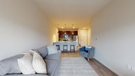 Located at 102 N Madison St in Waunakee, WI, this single-floor residence offers a thoughtfully designed open-concept layout with modern finishes throughout. The living area provides a welcoming atmosphere, featuring light wood-style flooring, neutral tones, and large windows with a sliding glass door that invites natural light and offers views of the surrounding area. The space flows seamlessly into the kitchen, which serves as a functional centerpiece of the unit. The kitchen is equipped with dark-toned cabinetry, stainless steel appliances including a refrigerator, range, and microwave, and a generous island with a white countertop and bar seating for multiple guests — illuminated by stylish pendant lighting overhead. The bedroom is a comfortable retreat with plush carpeting, a ceiling fan, and a well-sized closet with built-in shelving for ample storage. The bathroom features dark vanity cabinetry, a white countertop, and light wood-style flooring, offering a clean and contemporary feel. Throughout the residence, the consistent use of neutral colors, modern fixtures, and quality materials creates a cohesive and inviting living environment well-suited for everyday comfort.