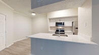 Located at 540 Carillon Pkwy in Saint Petersburg, Florida, this single-story residence offers a well-designed, open-concept layout with modern finishes throughout. The kitchen serves as a central hub of the home, featuring a large quartz-topped island with an undermount sink, white cabinetry, and a full suite of stainless steel appliances including a refrigerator, range, and over-the-range microwave. The kitchen flows seamlessly into the living area, which is finished with rich, dark hardwood-style flooring and neutral-toned walls that create a warm, inviting atmosphere. Crown molding adds a refined architectural detail to the main living spaces. A sliding glass door in the living area floods the room with natural light and provides access to the outdoors. The bedroom is generously proportioned, outfitted with the same hardwood-style flooring, a ceiling fan, and a window that brings in additional natural light. A dedicated in-unit laundry area houses a full-size Whirlpool front-loading washer and includes overhead shelving for storage. The home's single-floor layout ensures easy accessibility and cohesive flow between all areas, making it a practical and comfortable residence in the heart of Saint Petersburg.