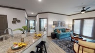 This single-story residence at Victory Knoll offers a thoughtfully designed open-concept layout that seamlessly connects the kitchen, dining, and living areas. The kitchen is a standout feature, showcasing dark espresso cabinetry paired with granite countertops, stainless steel appliances, and a generous island with bar seating — all set atop light wood-look flooring that extends throughout the main living areas. Crown molding with dark trim accents frames each room, lending a polished, cohesive aesthetic.

The living room is spacious and inviting, highlighted by a ceiling fan, large framed double doors that introduce natural light, and direct access to an outdoor area. A dedicated dining nook provides an intimate setting for meals, accented by bold botanical artwork and dark trim detailing.

The bedrooms offer comfortable retreats, each featuring plush carpeting, ceiling fans or ample lighting, and large windows dressed with blinds and curtains that allow natural light to fill the rooms. The primary bedroom is particularly well-proportioned, accommodating substantial furniture while maintaining an airy feel. Throughout the residence, neutral wall tones, quality finishes, and cohesive design elements create a warm and functional living environment.