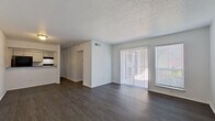 This single-story unit is designed with a clean, functional layout that maximizes the available living space. Throughout the unit, dark hardwood-style flooring provides a cohesive and contemporary look, contrasting with the crisp white walls and white baseboards found in every room.

The open living area serves as the heart of the unit, featuring a textured ceiling and a sliding glass door flanked by a large window, allowing abundant natural light to fill the space. The layout visible from the living area reveals a clear sightline to the adjacent kitchen, which is appointed with white cabinetry, granite-style countertops, a subway tile backsplash, and black appliances including a refrigerator, electric range, and dishwasher, along with a double-basin sink.

The bedroom is a well-proportioned space equipped with a ceiling fan and a large window for natural light. A walk-in closet offers generous storage capacity. An additional room with a ceiling fan provides flexible use as a second bedroom or den.

The bathroom features a full tub-shower combination with white tile surround and chrome fixtures, maintaining the unit's clean and consistent aesthetic throughout.