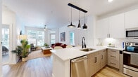 This thoughtfully designed single-floor residence offers 2 bedrooms and 3 bathrooms within a bright, modern layout. The open-concept living and kitchen area serves as the heart of the home, where light hardwood flooring, white walls, and large windows combine to create an airy, welcoming atmosphere. A ceiling fan enhances comfort in the living room, which receives generous natural light and offers views of the surrounding exterior.

The kitchen is outfitted with two-tone cabinetry — white upper cabinets paired with light wood lower cabinets — complemented by white quartz countertops, a subway tile backsplash, and a full suite of stainless steel appliances. A peninsula with pendant lighting above provides additional workspace and separates the kitchen from the living area.

Both bedrooms feature carpeted flooring, large windows with exterior views, and ceiling fans. The primary bedroom benefits from a dedicated walk-in closet with built-in shelving. The bathrooms are finished with large-format light tile, white vanities with illuminated mirrors, and soaking tub/shower combinations. Two closets provide practical storage throughout the residence.