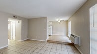 This single-floor, 2-bedroom, 1-bathroom residence offers a practical and straightforward layout designed to maximize its comfortable footprint. The living area features light-toned ceramic tile flooring and neutral beige walls, creating a clean, open feel. A ceiling fan overhead provides air circulation, while a wall-mounted HVAC unit offers climate control. The space flows seamlessly toward the kitchen, which is separated by a partial partition with built-in shelving. The kitchen is equipped with white cabinetry, a double-basin sink, and a full-size refrigerator, all set on matching tile flooring with a textured ceiling above.

Both bedrooms are carpeted in warm beige tones and feature ceiling fans with light fixtures. Natural light enters through windows fitted with blinds, casting bright, airy light across the rooms. The bedrooms connect to the rest of the unit via a central hallway, which also provides access to two closets for convenient storage.

The bathroom includes a single-sink vanity with ample cabinet storage, a wall mirror, and a tub-shower combination finished with tan ceramic tile surround. The tile flooring continues throughout the bathroom, maintaining a cohesive aesthetic. Overall, the space presents a clean, functional environment with consistent neutral tones throughout.