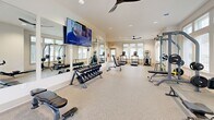 Located at 1018 Catalyst Blvd in Charlotte, NC, this fitness center offers a spacious, thoughtfully designed exercise facility spread across a single floor. The space is divided into distinct workout zones, each tailored to a different training style, creating a comprehensive gym experience.

The strength training area features floor-to-ceiling mirrors, a wall-mounted flat-screen TV, a full dumbbell rack with adjustable benches, and a cable machine system. Durable speckled rubber flooring provides both safety and comfort underfoot. Overhead, sleek black ceiling fans maintain airflow throughout the space.

A separate functional training room boasts light hardwood-style flooring and large, multi-pane windows that flood the area with natural light and offer outdoor views. This open zone accommodates a stationary bike, BOSU ball, step platforms, and other versatile training accessories — ideal for yoga, stretching, or low-impact workouts.

The cardio zone is lined with oversized windows on multiple walls, creating a bright and airy atmosphere. Treadmills, rowing machines, and additional strength equipment are neatly arranged to maximize floor space. Recessed lighting and ceiling fans throughout ensure consistent comfort during any workout.

The overall ambiance is clean, modern, and welcoming, with a neutral color palette of whites and warm beiges enhancing the sense of openness across the entire facility.