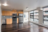 This single-floor unit offers a well-designed open-concept layout that seamlessly connects the kitchen and living areas, creating a functional and inviting space. Rich, dark hardwood flooring runs throughout, providing warmth and continuity across every room.

The kitchen is a standout feature, equipped with a full suite of stainless steel appliances including a refrigerator, electric range, microwave, and dishwasher. Light maple cabinetry provides ample storage, while a classic subway tile backsplash in soft blue-grey adds a contemporary touch. Track lighting overhead ensures excellent task illumination.

The open living area benefits from a large corner window that floods the space with natural light and frames views of the surrounding urban landscape, including tree canopies and city streetscapes. The clean, neutral wall tones enhance the brightness and sense of openness throughout.

The bathroom is cleanly appointed with white tile surrounding a full soaking tub and shower combination, a pedestal sink, and a wall mirror, offering a simple and functional design. A separate entry foyer provides a practical transition space upon arrival.

Overall, this unit presents a cohesive and modern aesthetic with practical finishes, abundant natural light, and an efficient, open floor plan well-suited for everyday living.