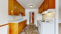 This single-floor unit offers a practical and straightforward layout designed for comfortable everyday living. The galley-style kitchen is lined on both sides with warm honey-toned wood cabinetry, providing generous upper and lower storage throughout. White appliances, including a coil-burner electric range with overhead ventilation and a full-size refrigerator, are neatly integrated into the space. A double-basin sink sits beneath the cabinetry on the opposing wall, and durable stone-patterned flooring runs the length of the kitchen. A doorway at the far end connects the kitchen to the rest of the unit.

The living area is generously proportioned, featuring neutral wall-to-wall carpeting, crown molding, and a sliding glass door that opens to a private balcony with outdoor views. The bedrooms continue the carpeted flooring and include closets with louvered bifold doors for organized storage. Each bedroom benefits from natural light through sliding or standard windows.

The bathroom is well-appointed with a wood-toned vanity, a wide countertop sink, a large mirror, white wall tile surrounding the tub and shower area, and a classic mosaic tile floor. Baseboard heating is present throughout, ensuring consistent warmth. The overall layout, visible in the 3D floor plan, reflects a compact yet efficient design.