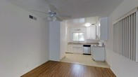 This single-floor residence offers a clean, functional layout that seamlessly connects the living area to the kitchen. The living space features warm wood-style flooring and is equipped with a ceiling fan with light fixture, adding both comfort and practicality. A textured ceiling completes the room's classic character.

The kitchen is finished in a bright, all-white palette with white cabinetry providing ample storage. It is equipped with a white electric range and a stainless steel dishwasher, and features a stainless steel sink set beneath a window that allows natural light to fill the space. Light tile flooring in the kitchen creates a clear visual distinction from the adjoining living area. A wall-mounted light fixture above the sink adds focused task lighting.

The open passthrough between the living room and kitchen enhances the sense of connectivity throughout the home, making the overall layout feel spacious and easy to navigate. The neutral color scheme across both spaces — white walls, white cabinetry, and light surfaces — creates a bright, airy ambiance throughout. This well-maintained, single-story home is well-suited for those seeking a straightforward and comfortable living environment.