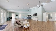 Located at 120 Ridgewood Dr in Raleigh, NC, this single-floor property offers an expansive, open-concept layout bathed in natural light and defined by soft seafoam-green walls and warm hardwood-style flooring throughout. The generous main living area is anchored by a striking stone fireplace and flanked by large French doors that open to an outdoor pool area, seamlessly blending indoor and outdoor living. Soaring vaulted ceilings with skylights and dual ceiling fans enhance the airy, open atmosphere of the space.

A dedicated workspace with desks and seating provides a functional office area within the main room, while a stylish lounge area with modern sectional seating adds comfort and versatility. The bar-style counter with seating serves as a natural divider between the living and kitchen areas. The fully equipped kitchen features granite countertops, white shaker cabinetry, a decorative tile backsplash, stainless steel appliances, and ample counter space, making it well-suited for both everyday use and entertaining. A white armoire adds a charming architectural accent near the entry. Together, these elements create a bright, welcoming, and highly functional single-level space.