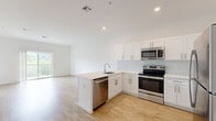 This single-floor unit offers a clean, modern aesthetic defined by bright white walls, light-toned luxury vinyl plank flooring, and an abundance of natural light throughout. The open-concept layout connects the kitchen directly to the living area, creating a seamless and functional flow. The kitchen is well-appointed with white shaker-style cabinetry, a geometric hexagonal tile backsplash, light quartz countertops, and a peninsula with an integrated sink. A full suite of stainless steel appliances — including a refrigerator, electric range, over-the-range microwave, and dishwasher — adds a polished, contemporary touch. The living area is spacious and bright, featuring sliding glass doors that open to a private balcony with views of lush, mature greenery. The bedrooms are finished with neutral carpet and large windows that frame scenic outdoor views of surrounding trees and open green space, filling each room with natural light. The bathroom includes a full soaking tub with shower, wood-look tile flooring, and crisp white finishes. Recessed lighting throughout the unit ensures consistent, even illumination, while the overall design palette of whites and warm wood tones creates a cohesive, inviting atmosphere.
