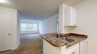 Located at 100 Town Walk Dr in Hamden, Connecticut, this single-floor residence offers a well-organized layout designed for comfortable everyday living. The open-concept kitchen and living area serves as the heart of the home, where a peninsula counter with dark granite-style laminate countertops and a stainless steel sink connects the two spaces seamlessly. The kitchen is equipped with white cabinetry, a tile backsplash, a gas range, and a full-size refrigerator, all set on easy-to-maintain wood-look flooring. The adjacent living area features plush carpeting, neutral white walls, and a large window that allows natural light to fill the room, as well as a sliding glass door that opens to a private balcony overlooking lush greenery. The carpeted bedroom offers generous proportions, highlighted by a wide triple-pane window framing tranquil outdoor views. A spacious walk-in closet serves the bedroom, outfitted with wire shelving and hanging rods along multiple walls for ample storage. The bathroom features a tub-shower combination and a vanity with cabinet storage. Textured ceilings and a consistent neutral color palette throughout create a clean, cohesive ambiance across the entire residence.