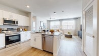This single-floor residence offers a clean, contemporary design with a bright, open-concept layout that seamlessly connects the kitchen, dining, and living areas. The kitchen is a standout feature, showcasing white shaker cabinetry, granite countertops, a large center island with bar seating and an integrated dishwasher, and stainless steel appliances including a French door refrigerator. Light wood-style flooring runs throughout the home, contributing to a cohesive and airy aesthetic. The living area benefits from large windows dressed with sheer curtains, allowing generous natural light to fill the space, and is equipped with a ceiling fan for year-round comfort. Both bedrooms are comfortably sized, with the primary bedroom offering a window with exterior views and its own walk-in closet outfitted with wire shelving systems. A second walk-in closet serves the additional bedroom. The two full bathrooms feature white cabinetry, granite-topped vanities, and tiled tub-shower combinations with marble-style surrounds. Recessed lighting and clean neutral tones throughout create a modern, move-in-ready atmosphere well suited for everyday living.