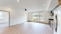Located at 3074 W Seltice Way in Coeur d'Alene, Idaho, this thoughtfully designed single-floor unit offers a clean, modern aesthetic defined by crisp white walls, light-toned luxury vinyl plank flooring, and an abundance of natural light. The open living area is a standout feature, anchored by large sliding windows and a glass door that frame views of the surrounding landscaped grounds, while recessed lighting and a ceiling fan enhance the bright, airy atmosphere. A wall-mounted HVAC unit provides efficient climate control throughout the main living space.

The kitchen is outfitted with a contemporary two-tone design, combining warm wood-grain lower cabinetry with matte gray upper cabinets. Stainless steel appliances — including a range, over-the-range microwave, dishwasher, and French door refrigerator — complement the dark countertops and black hardware throughout.

The bedroom is carpeted for comfort, featuring a large sliding window that brings in natural light and outdoor views. The bathroom presents a clean, modern design with a wood-grain vanity, gray countertop, undermount sink, black fixtures, pendant lighting, and a full tub-shower combination with white tile surround. The unit's cohesive, minimalist design creates a calm and functional living environment.