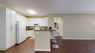 Located at 1500 White Birch Terr in Fremont, California, this single-floor residence offers a well-designed layout with a cohesive blend of function and comfort throughout. The kitchen is a standout feature, outfitted with crisp white cabinetry, dark countertops, and a full suite of white appliances including a refrigerator, electric range, and over-the-range microwave. Rich wood-look flooring runs throughout the kitchen and living areas, adding warmth and continuity to the space. A peninsula island with a dark countertop provides additional prep space and doubles as a casual dining area, accommodated by white bar-height seating. The open layout connects the kitchen seamlessly to the living area, which benefits from natural light streaming through vertical-blind-covered windows and is equipped with a ceiling fan. The bedroom features plush carpeting, neutral walls, and direct access to a closet area, creating a calm and functional retreat. The full bathroom includes a tub-shower combination with tile surround, a white vanity with dark countertop, a large mirror, and wood-look flooring. A dedicated in-unit laundry closet houses a full-size washer and dryer with overhead shelving, adding everyday convenience to this practical and well-appointed residence.