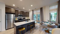 Located at 59 2nd Ave in Raritan, New Jersey, this single-floor residence offers a thoughtfully designed open-concept layout with contemporary finishes throughout. The kitchen is a standout feature, equipped with dark espresso cabinetry, stainless steel appliances including a refrigerator, microwave, and gas range, and a large center island topped with a crisp white quartz surface. Gold-accented bar stools add a stylish touch, while the adjacent dining area benefits from generous natural light streaming through floor-to-ceiling windows dressed with layered roller shades and grommet curtains. Light wood-style flooring flows seamlessly across the main living areas, enhancing the sense of openness. The space includes two well-proportioned bedrooms, each featuring large windows with outdoor views of lush greenery, providing a tranquil atmosphere. One bedroom offers direct access through a set of full-height windows, while the other benefits from corner windows that maximize natural light. The bathroom is finished with neutral tile, a soaking tub and shower combination, a dark wood vanity with a white countertop, and a frameless mirror. Recessed lighting throughout the home ensures a clean, modern aesthetic. Overall, the residence combines functional design with refined details in a well-lit, inviting environment.