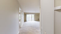 This single-floor residence offers a thoughtfully designed layout with a neutral color palette, plush wall-to-wall carpeting throughout the living areas and bedroom, and tile flooring in the kitchen and bathroom. The open living and dining area is generously proportioned, bathed in natural light through large sliding glass doors that lead to a private balcony overlooking lush greenery. A wide picture window in the secondary living area further enhances the sense of openness and connection to the outdoors. The kitchen features abundant white cabinetry with wood trim, dark laminate countertops, a stainless steel sink, and black appliances including an electric range, over-the-range microwave, and dishwasher. A convenient pass-through window connects the kitchen to the living space, adding an open, airy feel. The bedroom is spacious and bright, with access to a closet with louvered doors and a hallway leading to additional rooms. The bathroom is finished with tile flooring, a vanity with dark countertops, and a shower-tub combination with glass sliding doors. Clean white trim and warm beige walls throughout create a cohesive, welcoming ambiance suited for comfortable everyday living.