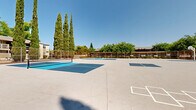 Located at 8079 Sunrise East Way in Citrus Heights, California, this outdoor recreational facility offers a well-appointed multi-sport court complex designed for active community use. The space features multiple pickleball courts with vibrant blue and teal court surfaces, clearly marked boundary lines, and regulation nets — ideal for both casual play and organized matches. A full basketball court with a standard hoop and painted key completes the athletic offerings, providing versatile options for a range of sports activities.

The entire complex is enclosed by a sturdy chain-link perimeter fence, ensuring a secure and defined play environment. Court lighting poles are positioned throughout the facility, extending the usability of the courts into evening hours. The aerial perspective reveals the thoughtful layout of the courts, making efficient use of the expansive paved surface area.

Tall cypress trees and mature deciduous trees line the perimeter, providing natural shade and a pleasant green backdrop under the bright California sky. Surrounding residential buildings and landscaped shrubs frame the facility, situating it within a neighborhood setting. The open-air design, clear sightlines, and well-maintained surfaces make this a functional and inviting recreational destination for the local community.