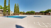 Located at 8079 Sunrise East Way in Citrus Heights, California, this outdoor recreational facility offers a well-appointed multi-sport court complex designed for active community use. The space features multiple pickleball courts with vibrant blue and teal court surfaces, clearly marked boundary lines, and regulation nets — ideal for both casual play and organized matches. A full basketball court with a standard hoop and painted key completes the athletic offerings, providing versatile options for a range of sports activities.

The entire complex is enclosed by a sturdy chain-link perimeter fence, ensuring a secure and defined play environment. Court lighting poles are positioned throughout the facility, extending the usability of the courts into evening hours. The aerial perspective reveals the thoughtful layout of the courts, making efficient use of the expansive paved surface area.

Tall cypress trees and mature deciduous trees line the perimeter, providing natural shade and a pleasant green backdrop under the bright California sky. Surrounding residential buildings and landscaped shrubs frame the facility, situating it within a neighborhood setting. The open-air design, clear sightlines, and well-maintained surfaces make this a functional and inviting recreational destination for the local community.