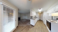This single-floor residence offers a practical and comfortable layout designed for everyday living. The open-concept kitchen flows directly into the living area, creating a connected and functional space. The kitchen is outfitted with white cabinetry, dark countertops, a double-basin sink, and white appliances including a coil-burner range and refrigerator. Wood-look flooring runs throughout the kitchen and entry areas, providing durability and easy maintenance.

The living room is carpeted and anchored by a classic fireplace with a white mantle and dark surround, offering a warm focal point for the space. Natural light enters through a windowed exterior door, adding brightness to the open area.

The bedrooms are carpeted and feature neutral wall tones, natural light from windows with blinds, and sliding or hinged closet doors providing ample storage. One bedroom includes a baseboard heater, indicating individual room climate control.

Two full bathrooms are included, each featuring a full-sized soaking tub with an overhead shower, white surround walls, chrome fixtures, and wood-look flooring. The clean, neutral finishes throughout the residence create a calm and move-in-ready atmosphere suited to a variety of living arrangements.