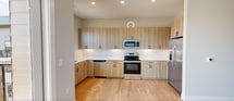 This 530-square-foot, one-bedroom, one-bathroom apartment at 4362 Watermark Dr in Wilmington, NC offers a clean, modern aesthetic throughout its single-floor layout. Light wood-look flooring flows consistently across every room, creating a warm and cohesive feel. The well-appointed kitchen is a standout feature, showcasing light wood flat-front cabinetry extending to the ceiling, crisp white quartz countertops, a white subway tile backsplash, matte black hardware, and a full suite of stainless steel appliances including a range, microwave, dishwasher, and refrigerator. A window above the sink fills the space with natural light. The 160-square-foot primary bedroom is bright and open, with neutral gray walls and direct access to both a dedicated closet with built-in shelving and a private bathroom. The bathroom features a large walk-in glass-enclosed shower with matte black fixtures, a vanity with wood cabinetry, and a framed mirror. A balcony off the unit offers expansive views of the surrounding landscaped grounds, a pond, and the broader Wilmington scenery under open skies, adding a notable outdoor dimension to this well-designed residence.