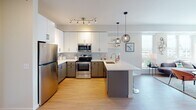 Located at 1711–1725 Nicollet Ave in Minneapolis, this single-floor unit offers a well-designed open-concept layout with modern finishes throughout. Light-toned hardwood flooring runs continuously across the living, kitchen, and bedroom areas, creating a cohesive and airy feel.

The kitchen is a standout feature, equipped with stainless steel appliances including a refrigerator, range, and microwave. Two-tone cabinetry pairs white upper cabinets with gray lower cabinets, complemented by a geometric patterned tile backsplash and white quartz countertops. A peninsula with seating extends into the living area, making it ideal for casual dining or entertaining. Stylish globe pendant lights hang above, adding a contemporary touch.

The bedroom is bright and spacious, benefiting from a large window that frames views of the Minneapolis skyline and surrounding greenery. A ceiling fan adds practical comfort, while neutral wall tones keep the atmosphere calm and versatile.

The bathroom features a bold design contrast, with a dark accent wall set against white quartz countertops, gray cabinetry, and a wide vanity mirror with integrated lighting. A shower-tub combination completes the space.

The overall layout, visible in the 3D overview, flows efficiently from the entry through the open living and kitchen area to the private bedroom and bathroom, making excellent use of the available space.