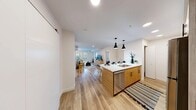 Located in Calgary, AB, this thoughtfully designed two-bedroom, two-bathroom residence offers a modern, open-concept layout finished with warm light wood flooring and crisp white walls throughout. The kitchen is a standout feature, showcasing natural wood cabinetry, stainless steel appliances, and a generous island with a white quartz countertop that seats multiple guests. Sleek black pendant lights hang above the island, adding a contemporary accent. The kitchen flows seamlessly into the dining area and living room, creating a cohesive social space. The living room benefits from large windows dressed with layered roller blinds, allowing for flexible light control and a bright, airy atmosphere. The primary bedroom is a calm retreat with a sizable window, the same warm-toned flooring, and neutral décor. The second bedroom offers comparable comfort and natural light. Both bathrooms are cleanly finished, each featuring a wood-toned vanity with a white countertop, framed mirror, and light-bar illumination. A dedicated dining nook and a closet with a sliding barn-style door add practical versatility. The unit's consistent use of natural wood tones, white surfaces, and modern fixtures gives the entire space a cohesive, contemporary aesthetic well-suited to urban living.