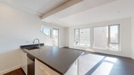 Located at 201 19th St in Oakland's Uptown neighborhood, this two-story residence showcases a clean, modern aesthetic throughout. The entry opens to rich dark hardwood flooring that flows through the main living areas, anchoring the contemporary design. Exposed ceiling beams add architectural character to the open-concept main floor, where the living and dining areas are bathed in natural light from large windows that frame urban Oakland views.

The kitchen is outfitted with stainless steel appliances, including a full-size refrigerator, gas range, and built-in microwave. White cabinetry with brushed gold hardware is complemented by a dark countertop island that doubles as a prep and dining surface. A hexagonal tile backsplash adds a subtle design detail. A dedicated lower-level kitchen and additional living area provide flexible functionality.

Carpeted bedrooms offer a quieter, softer feel, with one featuring an en-suite bathroom with pedestal sink. A walk-in closet with a full hanging rod provides generous storage. The full bathroom includes a tiled tub-shower combination, white cabinetry vanity with dark countertop, and large mirror. A keypad-secured entry door completes this well-appointed modern residence.