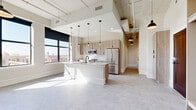 Located at 701 Douglas St in downtown Sioux City, Iowa, this thoughtfully designed two-bedroom, two-bathroom unit offers a contemporary urban living experience across a single, well-organized floor. The open-concept living and kitchen area serves as the heart of the unit, showcasing soaring ceilings with exposed industrial elements, large windows that flood the space with natural light, and sweeping views of the surrounding cityscape. The kitchen is equipped with stainless steel appliances, light wood cabinetry, white subway tile backsplash, and a prominent white island with pendant lighting above, creating both a functional and visually striking centerpiece. The bedrooms are well-proportioned and bright, with large windows offering outdoor views and built-in closet systems that maximize storage efficiency. Both bathrooms feature modern tilework, wood-toned cabinetry with matte black hardware, white countertops, and sleek fixtures. A dedicated laundry area and hallway add to the unit's practical layout. Throughout the space, a neutral color palette, consistent flooring, and clean architectural lines create a cohesive and polished aesthetic suited for contemporary urban living.