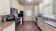 This two-story home presents a cohesive design aesthetic with warm neutral tones and a mix of flooring materials across its levels. The galley-style kitchen is well-appointed with white shaker cabinetry crowned with decorative molding, granite-style countertops, stainless steel appliances including a refrigerator, electric range, built-in microwave, and dishwasher, all set atop rich, dark hardwood-style flooring. A window at the end of the kitchen allows natural light to brighten the space.

The main living areas feature the same dark hardwood-style flooring and are fitted with ceiling fans and multiple doorways providing functional flow throughout. A half bath on the main level includes a vanity with granite-style counters and hardwood-style flooring. The upper-level bedrooms are carpeted and each include ceiling fans and windows fitted with horizontal blinds. The bathrooms are finished consistently, featuring white cabinetry, granite-style countertops, tub-shower combinations, and warm tile flooring. Throughout the home, white trim and soft neutral wall colors create a clean, unified appearance.