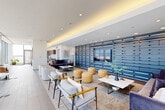 The Sky Pavilion & Lounge in Boston's Back Bay (02116) is a generously scaled, single-floor rooftop amenity space that seamlessly blends refined interior design with expansive outdoor access. Floor-to-ceiling curtain-wall glazing runs along the interior's longest elevation, flooding the space with abundant natural light while framing dramatic, unobstructed views of the Boston skyline, the Charles River, and surrounding neighborhoods.

Inside, the open-plan layout accommodates several distinct zones. A dining and collaboration area features large communal tables with contemporary upholstered seating. A sophisticated media lounge is anchored by a bold slate-blue slatted feature wall housing a large flat-screen display, complemented by low-profile sofas, accent armchairs, and golden leather ottomans arranged atop a textured area rug. Additional seating alcoves with swivel lounge chairs are positioned directly against the glass walls to maximize skyline vistas. Light-toned large-format tile flooring and recessed ceiling lighting maintain a clean, modern aesthetic throughout.

The space extends outdoors onto multiple wraparound terraces finished with stone pavers and glass-panel railings. These terraces are furnished with café-style dining sets, bar-height tables, and upholstered outdoor lounge suites, offering an elevated setting for open-air gatherings with panoramic views of Boston's iconic cityscape.
