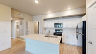 Located within The Farmstead community in Nampa, Idaho, this thoughtfully designed single-story home blends contemporary finishes with classic architectural details to create a welcoming and functional living environment. The open-concept kitchen serves as the heart of the home, showcasing a generous center island with a light quartz countertop, an undermount sink, and shaker-style white cabinetry that extends to the upper walls, providing ample storage. Black appliances, including a range, over-the-range microwave, refrigerator, and dishwasher, offer a striking contrast against the bright cabinetry. Light-toned luxury vinyl plank flooring flows throughout the main living and kitchen areas, lending a clean and cohesive feel. A standout feature of this home is the elegant board-and-batten wainscoting that adorns multiple walls, adding a refined, farmhouse-inspired character. Carpeted bedrooms offer a comfortable retreat, with windows that bring in natural light and neighborhood views. The bathroom features a quartz-topped vanity with clean white cabinetry and a large mirror, complemented by a walk-in closet conveniently accessible from the bath. Recessed lighting throughout ensures a bright, well-lit atmosphere across the entire home.