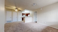 This single-floor residence offers a practical and functional layout across two bedrooms and two full bathrooms. The combined living room and kitchen area serves as the heart of the unit, where an open-concept peninsula separates the cooking space from the carpeted living area. The kitchen is equipped with rich walnut-toned cabinetry, white appliances including a range, refrigerator, and dishwasher, and light-toned countertops. A recessed skylight above the kitchen adds additional illumination to the space. The living room features a ceiling fan with light fixture, a textured ceiling, and a large window fitted with vertical blinds that allows natural light in. A front entry door opens directly into the living area, which provides a welcoming transition into the home. Both bedrooms are carpeted and feature neutral walls, with windows providing natural light and access to closet space. The two bathrooms are consistent in design, each featuring a tub-shower combination with white surround, tile flooring, and one bathroom includes a vanity with dark wood cabinetry and a granite-style countertop. A hallway connects the bedrooms and bathrooms, completing the efficient floor plan.