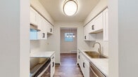 This single-floor unit showcases a thoughtfully updated interior with consistent wood-look vinyl plank flooring running throughout every room. The galley-style kitchen serves as a clear highlight, featuring white shaker cabinetry with matte black hardware, marble-look countertops, a stainless steel double-basin sink with a brushed gold faucet, a stainless steel range, and a dishwasher. Upper and lower cabinets provide ample storage, while a flush-mount ceiling light and a pass-through opening to the dining area—accented by a pendant light fixture—complete the space.

The living and dining areas are open and functional, benefiting from multiple windows that allow natural light to filter in. A wall-mounted air conditioning unit and baseboard heating ensure year-round comfort. The bedrooms are modestly sized, each with windows and textured ceilings, with one bedroom featuring a painted brick accent wall and two closets. The full bathroom is cleanly finished with white subway tile wainscoting, a shaker-style vanity with marble-look countertop, dark hardware, a combined tub and shower unit, and a well-lit mirror. The unit presents a cohesive, updated aesthetic throughout.