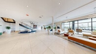 Located at 343 Mt Support Rd in Lebanon, NH, this expansive two-floor amenity facility — known as The Mrlek — offers a thoughtfully designed and well-appointed space for residents and guests alike. The ground floor makes an immediate impression with its grand, open-concept lobby clad in large-format porcelain tile flooring. Floor-to-ceiling black-framed glass windows flood the interior with natural light and provide views of the surrounding landscape. A sculptural staircase with sleek metal railings anchors the space, topped by a distinctive circular ceiling detail. Curated seating areas, lush potted plants, and bold contemporary artwork create a refined yet welcoming ambiance. A staffed reception desk near the entrance adds a hospitality-forward touch. A fully equipped fitness center features rubber flooring, extensive strength and cardio equipment, and full-length mirrors. A compact kitchenette with granite countertops, warm wood cabinetry, and a stone backsplash provides a convenient refreshment station. The upper floor continues the modern aesthetic with wide-plank hardwood flooring throughout. A spacious game and social lounge features a shuffleboard table, billiards table, and clusters of contemporary seating, all framed by panoramic windows. Hallways display large-scale original artwork, adding gallery-like character throughout.