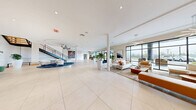 Located at 343 Mt Support Rd in Lebanon, NH, this expansive two-floor amenity facility — known as The Mrlek — offers a thoughtfully designed and well-appointed space for residents and guests alike. The ground floor makes an immediate impression with its grand, open-concept lobby clad in large-format porcelain tile flooring. Floor-to-ceiling black-framed glass windows flood the interior with natural light and provide views of the surrounding landscape. A sculptural staircase with sleek metal railings anchors the space, topped by a distinctive circular ceiling detail. Curated seating areas, lush potted plants, and bold contemporary artwork create a refined yet welcoming ambiance. A staffed reception desk near the entrance adds a hospitality-forward touch. A fully equipped fitness center features rubber flooring, extensive strength and cardio equipment, and full-length mirrors. A compact kitchenette with granite countertops, warm wood cabinetry, and a stone backsplash provides a convenient refreshment station. The upper floor continues the modern aesthetic with wide-plank hardwood flooring throughout. A spacious game and social lounge features a shuffleboard table, billiards table, and clusters of contemporary seating, all framed by panoramic windows. Hallways display large-scale original artwork, adding gallery-like character throughout.