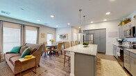 This single-floor residence offers a thoughtfully designed open-concept layout that seamlessly connects the kitchen, dining, and living areas. The kitchen is a standout feature, boasting gray shaker-style cabinetry, granite countertops, a subway tile backsplash, stainless steel appliances, and a spacious island with seating for multiple guests, illuminated by stylish pendant lights. The open dining area accommodates a full-sized round table and benefits from abundant natural light streaming through multiple windows and a private exterior door. The adjacent living room continues the warm, airy feel with large windows, wood-look flooring, and recessed lighting throughout. The primary bedroom is carpeted and well-lit, featuring a ceiling fan and generous window views of the outdoors. A second bedroom offers similar comfort with plush carpet and ample natural light. The primary bathroom includes a glass-enclosed walk-in shower with tile surround, while the secondary bathroom features a granite-topped vanity with blue cabinetry, a large mirror, and a tub-shower combination. A dedicated laundry area with stacked washer and dryer hookups rounds out this functional and elegant space.
