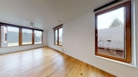 This thoughtfully designed single-floor space combines modern aesthetics with practical functionality throughout. Wide-plank hardwood floors in a warm natural oak tone run continuously through the living and sleeping areas, creating a cohesive and inviting atmosphere. Multiple large, wood-framed windows flood the interior with abundant natural light and provide views of the surrounding neighborhood rooftops, while roller shades offer privacy when needed. Baseboard heating units beneath the windows ensure comfort year-round.

The open-plan living area is generously proportioned, offering flexible arrangement possibilities, and flows seamlessly toward the kitchen at the far end. A ceiling fan serves the main living space. The kitchen is well-appointed with white cabinetry, wood-toned countertops, a white subway tile backsplash, and a full suite of stainless steel appliances including a built-in oven, cooktop, dishwasher, microwave, and refrigerator. A utility cart provides additional prep space and mobility.

The bathroom is finished in a clean, contemporary style with dark slate-look floor tiles, a white vanity with quartz countertop, chrome fixtures, and a glass-enclosed shower with white tile surround. In-unit laundry is also present. Overall, the space presents a bright, move-in-ready interior with a minimalist character.