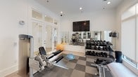 Located at 2211 Parklake Dr NE in Atlanta, Georgia, this fitness center is a well-appointed, single-level space designed to support a comprehensive workout experience. The interior features a clean, modern aesthetic with crisp white walls, recessed lighting, and a combination of light hardwood-style flooring and durable checkered rubber fitness flooring in the main exercise area.

The facility is equipped with a robust selection of Precor strength machines, a cable crossover system, and a full rack of dumbbells ranging across multiple weight increments, suitable for users of all fitness levels. A wall-mounted flat-screen television provides entertainment during workouts, while a large floor-to-ceiling mirror along one wall enhances the sense of space and allows for form monitoring. Stability and balance training accessories, including a BOSU ball and exercise ball, are also available.

Natural light filters into the space through multiple large windows fitted with roller shades, offering a bright and energizing atmosphere. Glass-paneled double doors with transom windows connect the strength training area to an adjacent cardio room, which is visible through the interior windows and contains additional treadmills and equipment. The overall design balances functionality with a polished, contemporary finish, making this fitness center a practical and well-maintained amenity.