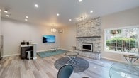 This thoughtfully designed single-floor space showcases a seamless open-concept layout that connects the living, dining, and kitchen areas with a cohesive modern aesthetic. Light-toned hardwood flooring flows throughout, lending warmth and continuity to the entire space.

The living area is anchored by a dramatic floor-to-ceiling stacked stone fireplace with a sleek linear electric insert and a solid mantel shelf, serving as a bold architectural focal point. Recessed lighting and a stylish chandelier complement the space, while large windows invite abundant natural light and views of lush outdoor greenery.

An expansive secondary living or flex area features a distinctive angled bay window with a built-in bench ledge and is accessible through elegant French doors, offering versatility for a variety of uses. This area is accented by contrasting warm taupe walls, adding depth and character.

The kitchen is efficiently designed with rich dark-toned cabinetry, stainless steel appliances, a mosaic tile backsplash, and a peninsula with a clean white countertop that provides both workspace and informal seating. A wall-mounted mini-split system ensures climate comfort throughout.

Overall, the space presents a polished, contemporary atmosphere with carefully curated design details that balance functionality and style.