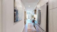 Located in Redmond, WA, this thoughtfully designed one-bedroom, one-bathroom residence offers a modern aesthetic with high-quality finishes throughout. The galley-style kitchen is a standout feature, outfitted with stainless steel appliances including a French door refrigerator, built-in microwave, electric range with a stainless hood, and a subway tile backsplash. Light wood cabinetry and white quartz countertops lend a clean, contemporary feel, while hardwood-style flooring runs seamlessly throughout the space. A hallway adorned with statement wall art connects the kitchen to the living area, where large sliding glass doors flood the room with natural light and open to a private balcony with courtyard views. The living room also features a wall-mounted mini-split system for year-round comfort. The bedroom is a cozy retreat with a sliding barn-style closet door revealing a walk-in closet, complemented by warm neutral tones and soft wall art. The bathroom features a full tub-shower combination with crisp white subway tile surround. Recessed lighting and a cohesive modern design palette tie every room together, making this a well-appointed urban residence in the heart of Redmond.