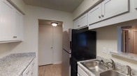This renovated single-floor residence offers a thoughtfully designed 1-bedroom, 1-bathroom layout with modern updates throughout. The living area is bright and open, featuring wood-style plank flooring and a sliding glass door with vertical blinds that provides natural light and outdoor views of surrounding greenery. A ceiling fan adds comfort and functionality to the space.

The kitchen is connected to the living area via a pass-through opening with a granite-style countertop bar, creating an open and interactive flow between the two spaces. The kitchen itself is well-equipped with white shaker-style cabinetry, granite-style countertops, a stainless steel double-basin sink, a refrigerator, electric range, and an over-the-range microwave. Light wood-style flooring extends throughout the kitchen and hallway.

The bedroom is a comfortable, carpeted room with two closets providing ample storage and a window that brings in natural light. The full bathroom features wood-look vinyl flooring, a white vanity with updated hardware, and a clean tub/shower combo with chrome fixtures. Neutral tones and clean finishes give the entire unit a fresh, move-in-ready feel.