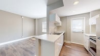 Located at 1736 N Hillside St in Wichita, Kansas, this efficiently designed single-floor unit makes smart use of its compact footprint. The open-concept layout connects the living area to the kitchen, creating a sense of spaciousness enhanced by neutral gray-toned walls, crisp white trim, and warm wood-look plank flooring that runs throughout the space.

The kitchen is a standout feature, thoughtfully designed with a central peninsula that doubles as a workspace and casual dining counter. White flat-front cabinetry lines the walls, complemented by a stainless steel sink, a stainless steel range, and a full-size refrigerator. A window above the sink area and an exterior door allow natural light to brighten the kitchen.

The living area is open and versatile, with clean walls, ample floor space, and a built-in closet nook, offering functional storage within the unit. The bathroom is finished with floor-to-ceiling white subway-style tiles, a walk-in shower with a chrome fixture, a wall-mounted vanity with sink, and a mirrored medicine cabinet. A frosted window provides natural light while maintaining privacy.

Overall, the unit presents a clean, modern aesthetic with practical finishes suited for efficient, comfortable living.