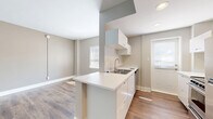 Located at 1736 N Hillside St in Wichita, Kansas, this efficiently designed single-floor unit makes smart use of its compact footprint. The open-concept layout connects the living area to the kitchen, creating a sense of spaciousness enhanced by neutral gray-toned walls, crisp white trim, and warm wood-look plank flooring that runs throughout the space.

The kitchen is a standout feature, thoughtfully designed with a central peninsula that doubles as a workspace and casual dining counter. White flat-front cabinetry lines the walls, complemented by a stainless steel sink, a stainless steel range, and a full-size refrigerator. A window above the sink area and an exterior door allow natural light to brighten the kitchen.

The living area is open and versatile, with clean walls, ample floor space, and a built-in closet nook, offering functional storage within the unit. The bathroom is finished with floor-to-ceiling white subway-style tiles, a walk-in shower with a chrome fixture, a wall-mounted vanity with sink, and a mirrored medicine cabinet. A frosted window provides natural light while maintaining privacy.

Overall, the unit presents a clean, modern aesthetic with practical finishes suited for efficient, comfortable living.