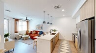 This thoughtfully designed one-bedroom, one-bathroom unit offers a functional and stylish single-floor layout. The open-concept kitchen and living area serves as the heart of the space, where a contemporary kitchen island with a white quartz countertop and undermount sink anchors the room. A trio of matte pendant lights hang above the island, complementing the warm wood-toned lower cabinetry, white upper cabinets, and stainless steel appliances, including a full-size refrigerator and range. Light wood-look flooring runs throughout, enhancing the bright, airy atmosphere created by white walls and recessed lighting.

The living area flows naturally from the kitchen and features a ceiling fan, large windows with blinds and curtain panels, and a glass-paned door providing additional natural light. The bedroom is a comfortable retreat, equipped with its own ceiling fan, a window, and carpet underfoot. It connects directly to the full bathroom, which features a wood-toned vanity with a white countertop, a framed mirror with black hardware, and a glass-enclosed shower with white subway tile. Adjacent to the bathroom is a walk-in closet with wrap-around shelving and hanging rods, offering generous storage.