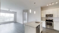 The Chestnutt offers a thoughtfully designed single-floor residence with a clean, contemporary aesthetic defined by a neutral gray-and-white color palette and durable wood-look flooring throughout the main living areas. The open-concept kitchen serves as a central focal point, showcasing white shaker cabinetry, a subway tile backsplash, stainless steel appliances — including a refrigerator, range, and microwave — and a large central island topped with stone-look countertops and an undermount sink. Pendant lighting above the island adds a refined finishing touch. The kitchen flows seamlessly into the living area, which is enhanced by a ceiling fan and access to a private balcony with outdoor views, inviting generous natural light through large windows with blinds. The bedrooms feature soft carpeting, ample natural light, and well-proportioned closet space. One bathroom includes a full tub-shower combination with white subway tile surround, a stone-top vanity with white cabinetry, and tile flooring. A walk-in closet with built-in shelving connects conveniently to the primary bath, providing practical organization. The overall ambiance is bright, clean, and move-in ready.