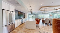 Located at 601 Industrial Blvd W in Waconia, Minnesota, this first-floor clubroom offers a spacious, open-concept layout designed for community gathering and entertaining. The space is finished with warm, neutral-toned flooring throughout and sage green walls that create a calm, welcoming ambiance.

The full-service kitchen is a standout feature, anchored by a large waterfall-edge quartz island with seating for multiple guests along one side. White shaker cabinetry lines the walls, complemented by a striking dark stacked-tile backsplash, stainless steel appliances including a French door refrigerator and dishwasher, and pendant lantern lighting overhead.

Adjacent to the kitchen, a generous dining area accommodates a full dining table and chairs, positioned alongside floor-to-ceiling sliding glass doors and a glass panel door that open directly to an outdoor deck. The deck features Adirondack-style seating and overlooks a lush, tree-lined landscape, flooding the interior with natural light and views of the surrounding greenery.

The lounge area offers comfortable seating arranged around a fireplace framed by a shiplap surround, built-in shelving, and a mounted television. A stylish chandelier anchors the space, while large windows continue the theme of abundant natural light. The overall design balances modern finishes with a warm, residential character ideal for a shared community setting.