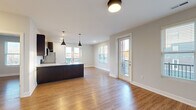 Located at 1011 Lusso Ave in Columbus, Ohio, this single-floor residence offers a well-designed, modern interior with a cohesive aesthetic throughout. The open-concept layout seamlessly connects the kitchen and living area, creating a spacious and functional living environment. The kitchen is a standout feature, equipped with dark espresso cabinetry, stainless steel appliances including a refrigerator, range, and microwave, a white quartz-topped island with an undermount sink, and a classic subway tile backsplash. Stylish pendant lighting above the island adds a contemporary touch. The living and dining area is bathed in natural light from multiple windows and a set of glass doors that open to a private balcony, offering views of the surrounding Columbus neighborhood. Warm hardwood-style flooring runs consistently throughout the unit, enhancing the sense of continuity. The bedrooms are well-proportioned, each featuring natural light from exterior-facing windows and ample closet space with double-door configurations. The bathroom is finished with a dark wood vanity, white quartz countertop, and a large mirror. Neutral gray walls and clean white trim provide a modern, move-in-ready finish throughout the entire space.