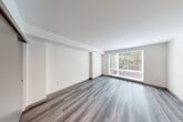 Located at 400 Queen Anne Ave N in Seattle, WA, this efficiently designed single-floor unit offers a thoughtfully laid-out living space with modern finishes throughout. The unit features warm-toned luxury vinyl plank flooring that runs continuously across all rooms, lending a cohesive and contemporary feel.

The living area is bright and open, anchored by a large window fitted with horizontal blinds that frame views of surrounding greenery, filling the space with natural light. Clean white walls and a smooth ceiling contribute to an airy, uncluttered atmosphere.

The galley-style kitchen is well-appointed with light wood cabinetry, white quartz countertops, a tile backsplash, and a full suite of stainless steel appliances including a refrigerator, electric range, built-in microwave, and dishwasher. A wall-mounted mini-split system provides climate control.

The combined bathroom and laundry area is a standout feature, offering a full bathtub and shower with matte black fixtures, a wood-toned vanity with quartz countertop, a large mirror, and a stacked washer and dryer unit — maximizing functionality within a compact footprint.

Two closets provide convenient storage, and the entrance corridor connects all areas of the unit in a clean, linear flow. This unit is ideal for those seeking a modern, move-in-ready space in the heart of Queen Anne.