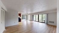 This single-floor residence offers a well-organized layout that balances open living spaces with comfortable private quarters. The expansive main living area is a standout feature, finished with light hardwood-style flooring that extends throughout and complemented by a textured ceiling. A wall of large sliding glass doors floods the space with abundant natural light and provides direct access to a balcony overlooking lush greenery, creating a seamless indoor-outdoor connection. A mirrored wall accent and ceiling fan add functional and visual interest to the living area. The kitchen is appointed with rich, warm-toned wood cabinetry, granite-look countertops, a double basin sink, and black appliances including a full-size refrigerator, offering ample storage and workspace. The bedrooms are carpeted for comfort and each features a dedicated closet with bi-fold louvered doors, providing generous storage. The bathroom includes a full soaking tub and shower combination with a glass door enclosure, white tile surround, and a mirrored medicine cabinet. Overall, the space presents a clean, functional, and well-lit environment with a practical floor plan suited for everyday living.