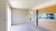 Located at 2299 N Silverbell Rd in Tucson, Arizona, this one-bedroom, one-bathroom unit offers a practical and efficient single-floor layout. The carpeted living room provides a comfortable gathering space and connects seamlessly to a pass-through kitchen, which features warm wood cabinetry, light countertops, stainless steel appliances including an electric range, over-the-range microwave, dishwasher, and a sink — all set over durable hardwood-style flooring. A built-in pantry with open shelving adds valuable storage to the kitchen area. The bedroom is a well-proportioned, carpeted retreat with a large window fitted with vertical blinds, allowing natural light to brighten the space. A closet in the bedroom houses a stacked in-unit washer and dryer, a convenient and practical feature. The bathroom is neatly appointed with a tiled tub-shower combination, a wood-vanity with sink, and hardwood-style flooring. Neutral tones and textured ceilings are consistent throughout, giving the unit a clean, cohesive aesthetic. A hallway connects the main living areas, contributing to the space's organized flow. This unit is well-suited for those seeking a streamlined, low-maintenance living space in Tucson.