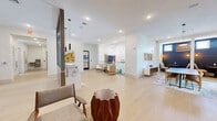 Located at 9030 SW 158th Ave in Miami, FL, this thoughtfully designed single-floor amenity space offers a generous and open layout that seamlessly blends functionality with contemporary style. Light wood-toned tile flooring flows throughout, unifying the living room and connecting hallways into a cohesive, inviting environment.

The central living area serves as the heart of the space, featuring a striking decorative partition with vertical wooden slats and pendant lighting that creates an elegant visual divide. Rattan accent chairs, sculptural wooden side tables, and carefully selected artwork contribute to a warm, curated aesthetic. A glass-railed mezzanine overlook adds architectural depth and visual interest, with a bold macramé wall installation and a geometric gold chandelier as standout decorative elements.

One hallway leads to a dedicated lounge area anchored by a sweeping floor-to-ceiling marble-effect mural in soft blues and earth tones, complemented by built-in bench seating, accent chairs, and a mounted display screen — ideal for gathering or relaxation. Black-framed glass doors line the corridor, allowing natural light to filter through.

An adjacent meeting or dining area features a large conference-style table beneath a woven rattan pendant light, framed artwork, and an intimate nook with navy blue accent walls and wall sconces. The overall ambiance is modern, polished, and welcoming, reflecting a refined Miami aesthetic.
