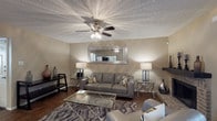 This single-story residence offers a well-organized layout across two bedrooms and two bathrooms, designed for comfortable everyday living. The living room serves as the focal point of the home, featuring rich hardwood-style flooring, a textured ceiling with a ceiling fan and light fixture, and warm neutral walls. A corner brick fireplace adds character and warmth, while a large decorative mirror mounted above the seating area enhances the sense of space. The room is well-lit with ambient lighting and benefits from natural light through slatted vertical blinds.

The kitchen is equipped with wooden cabinetry, granite-style countertops, and a black electric range, providing ample workspace and storage for everyday cooking needs.

Both bedrooms are carpeted and generously sized, each featuring multiple windows that allow for abundant natural light and outdoor views of surrounding greenery. Closet space is included in the bedrooms for practical storage. The bathrooms are finished with wooden vanities, granite-style countertops, and a tub-shower combination with clean white tile surrounds. Flooring in the bathrooms transitions to wood-style vinyl for easy maintenance. Overall, the home presents a cohesive, neutral aesthetic throughout.